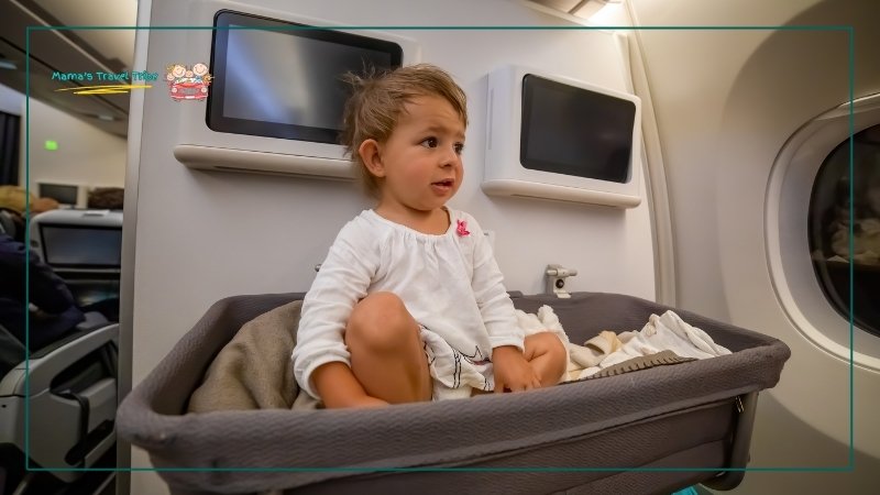book a bassinet. 1 year old sitting in an airplane bassinet. tips for flying with a 1 year old