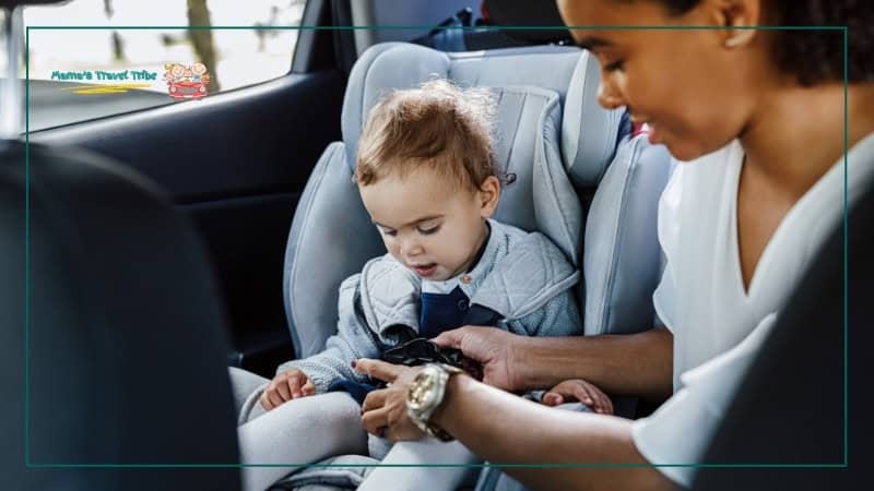 mother strapping baby in her car seat. Rental car, rideshare, and public transport each change the safety setup in different ways. Family Travel Safety Guide: Practical Safety Tips for Babies, Toddlers, and Young Kids